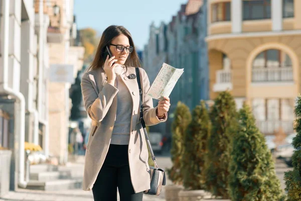 Ung vacker affärs kvinna med en res väska på den soliga staden gatan, flicka med turist karta pratar på mobil telefon — Stockfoto