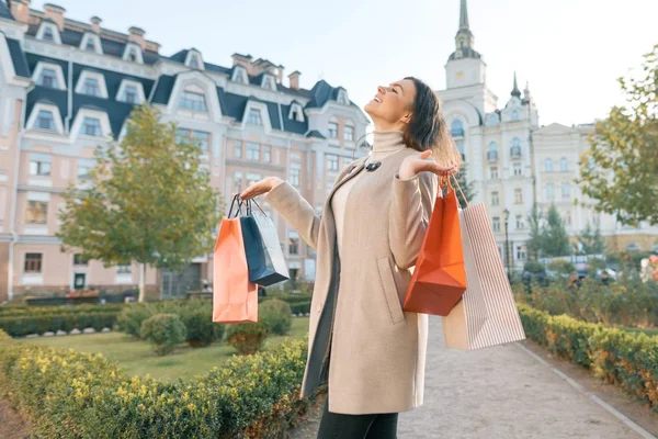 Junge lächelnde brünette Frau mit Einkaufstaschen, sonniger Stadthintergrund, goldene Stunde — Stockfoto