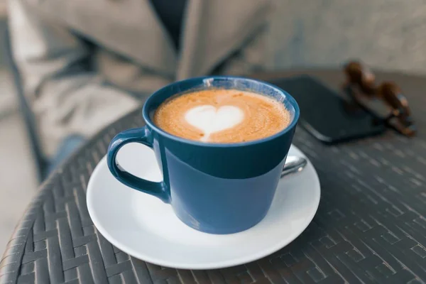 屋外のカフェでテーブルの上に青いカップにハートを持つコーヒーアート — ストック写真