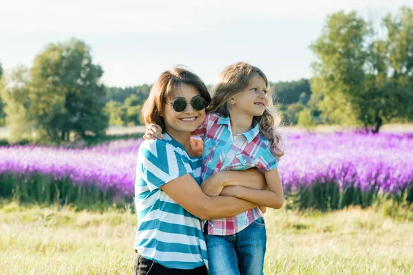 Leende mamma med sin lilla dotter omfattar promenader på naturen, bakgrund solig sommar dag lila lavendel fält — Stockfoto