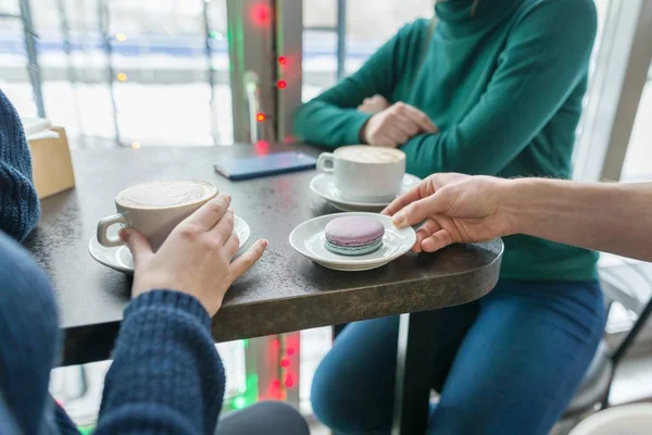 Primer plano de dos manos de las mujeres con tazas de café y macarrones en el plato en la mano del hombre en la mesa de piedra gris, fondo de la cafetería — Foto de Stock