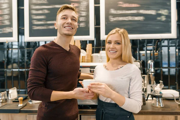 Happy smiling couple at the coffee shop counter, workers or owners with a cup of fresh art coffee looking at the camera. Small business, service, cafe — Stock Photo, Image