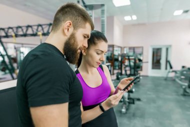 Spor salonunda kişisel antrenör ile konuşurken, smartphone içinde seyir ve tartışmaya genç kadın. Fitness, spor, eğitim, insanlar, sağlıklı yaşam konsepti