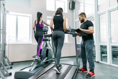 Genç gülümseyen fitness kadınlar ile kişisel antrenör salonunda treadmill atletik yetişkin bir adam. Eğitim, spor, takım çalışması, sağlıklı yaşam konsepti