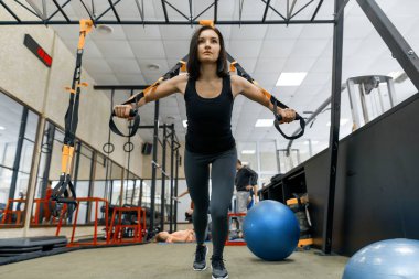 Genç güzel kadın CrossFit spor salonunda fitness askıları ile yapıyor. Eğitim, spor, fitness, insanlar kavramı.
