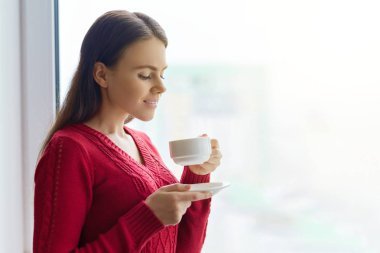 Hoş kokulu kahve, sıcak bir örme kazaklı pencerenin yakınındaki kadın zevk genç gülümseyen kadın