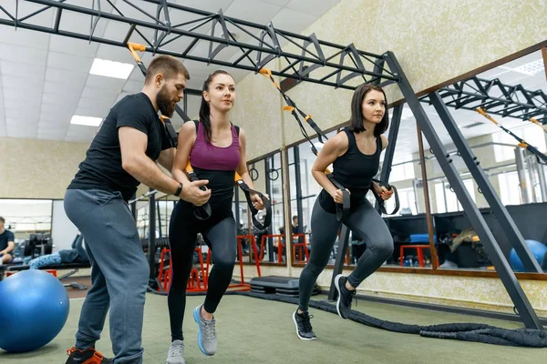 Fitness trainer coaching and helping women doing exercises on cross fit using straps system in gym. Sport, teamwork, training, people concept. — Stock Photo, Image