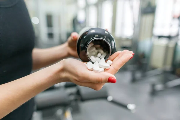 Primer plano de las manos de la mujer de fitness que muestra los suplementos deportivos y de fitness, cápsulas, pastillas, fondo del gimnasio. Estilo de vida saludable, medicina, suplementos nutricionales y concepto de personas — Foto de Stock