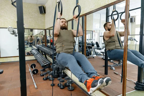 Muskulöser kaukasischer bärtiger Mann, der in gewichteter Weste in der Sporthalle Übungen macht, militärischer Stil — Stockfoto