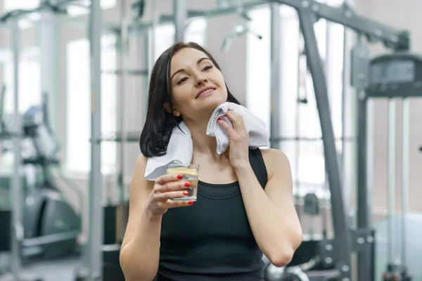 Portrait einer lächelnden Fitness-Frau mit einem Glas Wasser mit Zitrone, einer Frau in Sportbekleidung nach einem Fitnesskurs, die im Fitnessstudio Wasser trinkt — Stockfoto