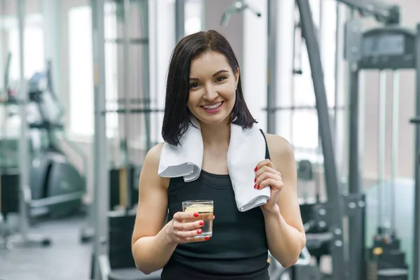 Portrait einer lächelnden Fitness-Frau mit einem Glas Wasser mit Zitrone, einer Frau in Sportbekleidung nach einem Fitnesskurs, die im Fitnessstudio Wasser trinkt — Stockfoto