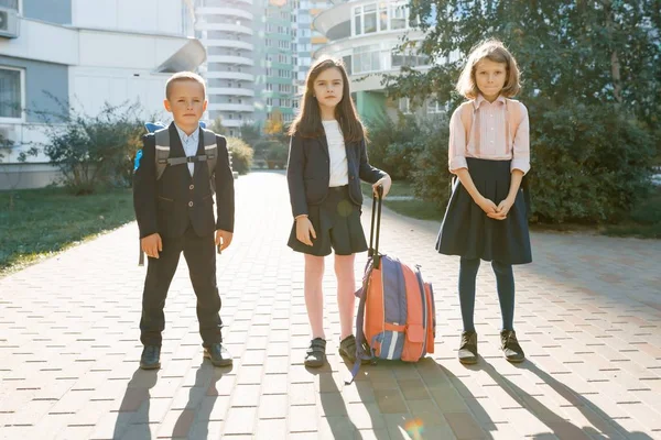Retrato al aire libre de escolares sonrientes en la escuela primaria. Un grupo de niños con mochilas se divierten, hablan. Educación, amistad, tecnología y concepto de personas — Foto de Stock