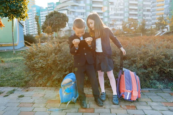 Alumnos de niños y niñas en primaria con una tableta digital. Fondo exterior, niños con bolsas escolares, mira la tableta. Educación, amistad, tecnología y concepto de personas — Foto de Stock