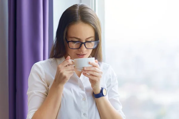 Retrato de joven empresaria en vasos con taza de café. Mujer bebiendo café cerca de la ventana de la oficina — Foto de Stock