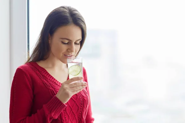 Молода дівчина в теплому в'язаному светрі зі склянкою води з лаймом. Вітамін здоровий напій в осінній зимовий сезон — стокове фото
