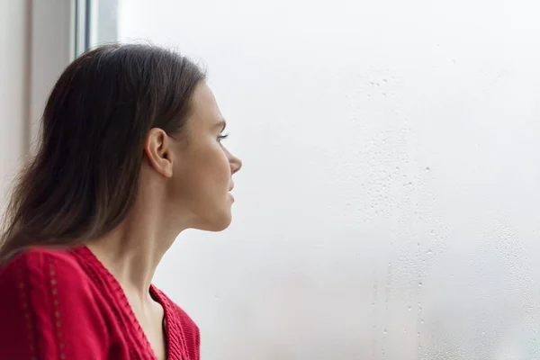 Genç kadın bir yağmurlu günde, kopya alanı pencereden dışarı bakarak — Stok fotoğraf