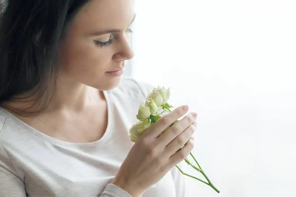 Молода брюнетка з білими трояндовими квітами, дівчина біля вікна з краплями — стокове фото