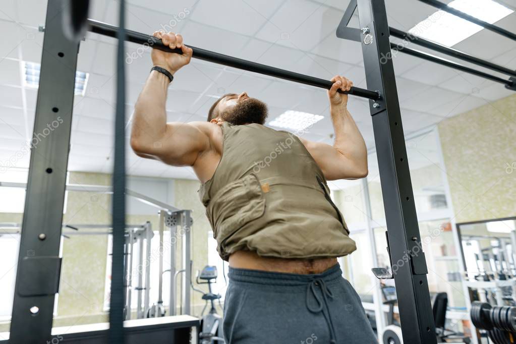 Military sport, muscular caucasian bearded adult man doing exercises in the gym dressed in bulletproof armored vest