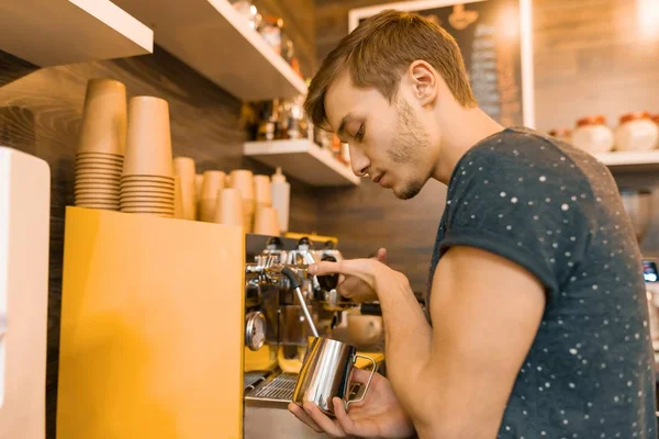 若い男性バリスタはコーヒー マシンの近くに飲み物を作る。コーヒー ショップ ビジネス コンセプト — ストック写真