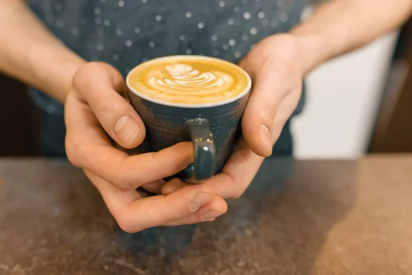 Primer plano arte latte. La taza del café fresco con la espuma y el dibujo en las manos del hombre —  Fotos de Stock