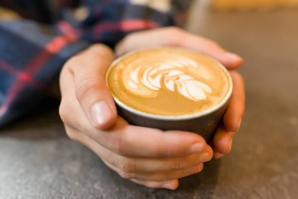 Primer plano arte latte. Taza de café fresco con espuma y dibujo en las manos de la mujer —  Fotos de Stock