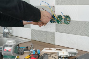 Tadilat ve inşaat mutfak, seramik duvar prizine yüklemek elektrikçiler el close-up profesyonel araçlar kullanarak döşer