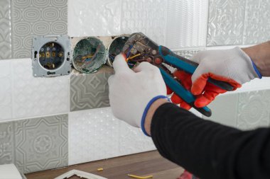 Renovation and construction in kitchen, close-up of electricians hand installing outlet on wall with ceramic tiles using professional tools clipart