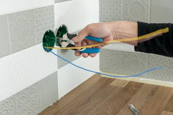 Renovatie en nieuwbouw in keuken, close-up van elektriciens hand stopcontact installeren op muur met keramische tegels met behulp van professionele gereedschappen — Stockfoto