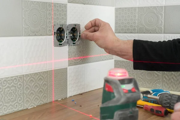 Elektryk Instalowanie gniazd elektrycznych za pomocą podczerwieni laser poziom. Remontowo -budowlane w kuchni — Zdjęcie stockowe