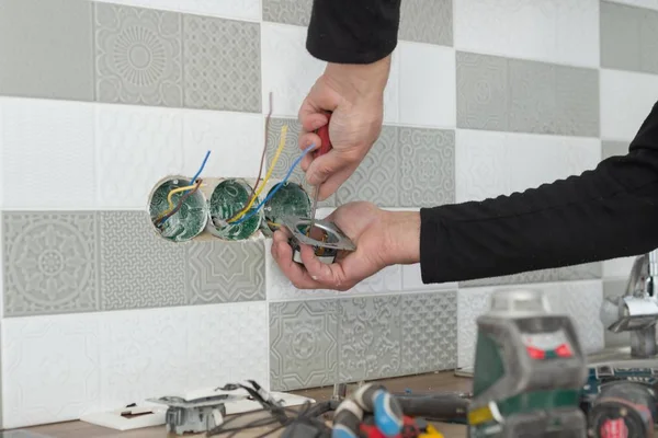 Renovação e construção na cozinha, close-up de eletricistas mão instalar tomada na parede com telhas cerâmicas usando ferramentas profissionais — Fotografia de Stock