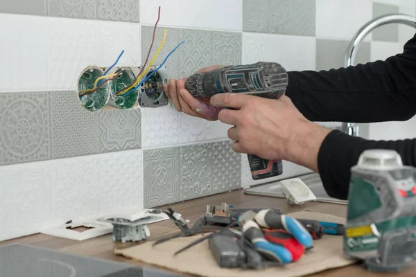 Renovação e construção na cozinha, close-up de eletricistas mão instalar tomada na parede com telhas cerâmicas usando ferramentas profissionais — Fotografia de Stock