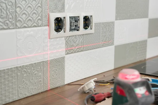 Eletricista usando o nível de laser infravermelho para instalar tomadas elétricas. Renovação e construção em cozinha — Fotografia de Stock