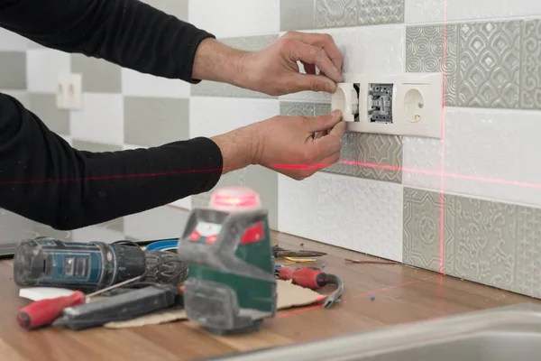 Elettricista che utilizza il livello laser a infrarossi per installare prese elettriche. Ristrutturazione e costruzione in cucina — Foto Stock