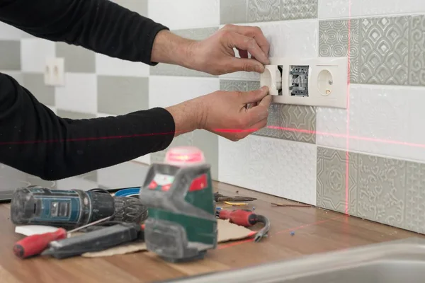 Eletricista usando o nível de laser infravermelho para instalar tomadas elétricas. Renovação e construção em cozinha — Fotografia de Stock