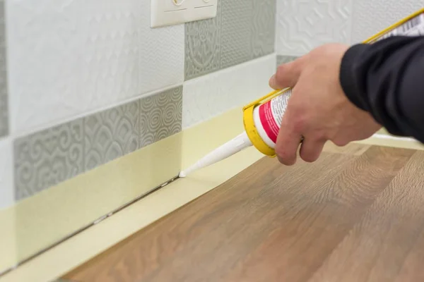 Applying silicone sealant with construction syringe. Worker fills seam between the ceramic tiles on the wall and kitchen worktop — Stock Photo, Image