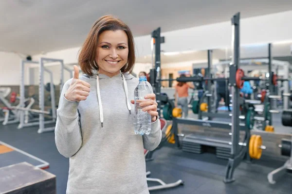 Reife Frau im Fitnessstudio mit Wasserflasche und zeigt ok Zeichen. Gesundheit Fitness Sport Alterskonzept — Stockfoto
