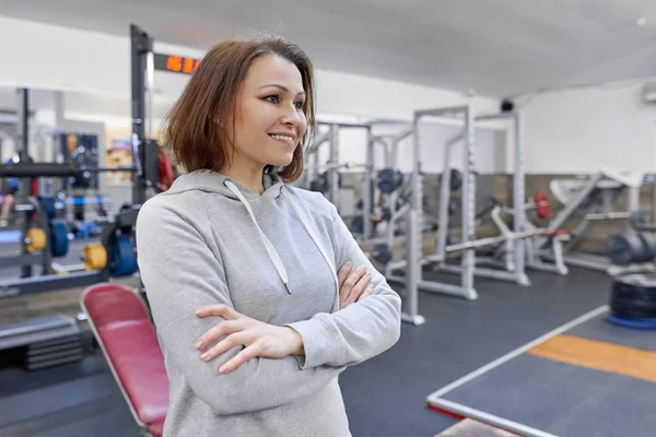 Retrato de mujer confiada de mediana edad sonriente con las manos dobladas en el gimnasio — Foto de Stock