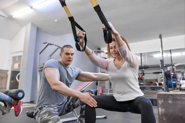 Reife Frau, die im Fitnessstudio mit Fitnessschlaufen trainiert. männlicher Instruktor unterstützt Frau mittleren Alters — Stockfoto