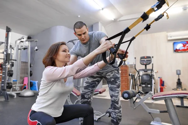 Starsza kobieta, ćwiczenia w siłowni przy użyciu fitness pasy pętle. Mężczyzna instruktor wspierające Kobieta w średnim wieku — Zdjęcie stockowe