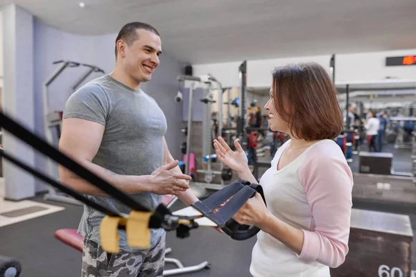 Istruttore di fitness e donna matura in palestra. Istruttore di sport maschile e donna di mezza età che parla e ride nel centro benessere — Foto Stock