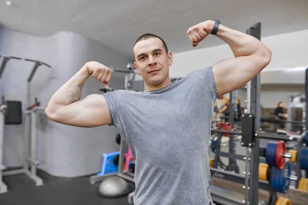Junger stark lächelnder muskulöser Mann im Fitnessstudio zeigt starke muskulöse Arme. — Stockfoto