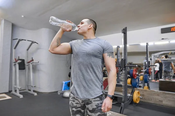 Junger kräftiger muskulöser Mann in Turnhalle trinkt Wasser aus Flasche — Stockfoto