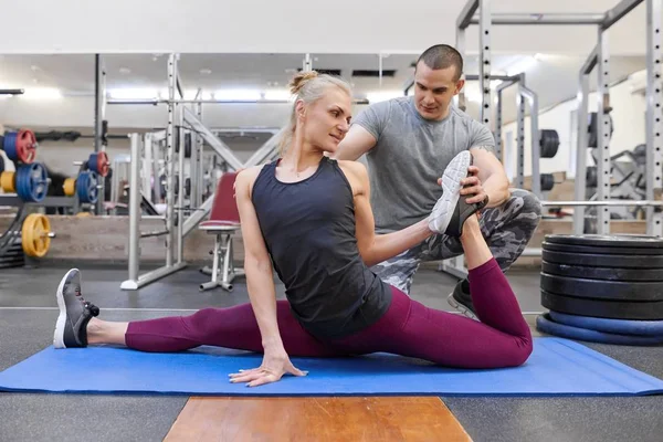Genç güçlü kas adam genç atletik kadın spor salonunda yoga mat uzanan yardım — Stok fotoğraf