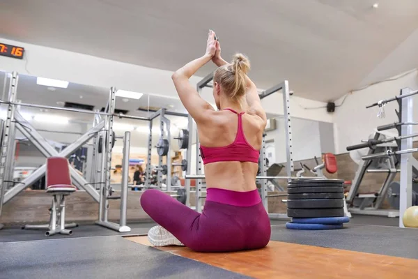 Young athletic muscular woman doing stretching workout in the gym, woman practicing yoga, view from the back