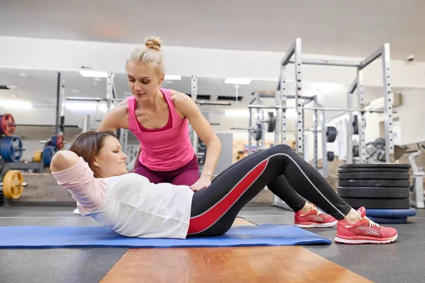 Middle-aged woman doing sports exercise in fitness center. Personal gym trainer assisting mature woman. Health fitness sport age concept — Stock Photo, Image