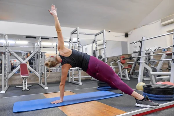 Young sporty blonde woman stretching body while doing yoga exercises at gym — Stock Photo, Image