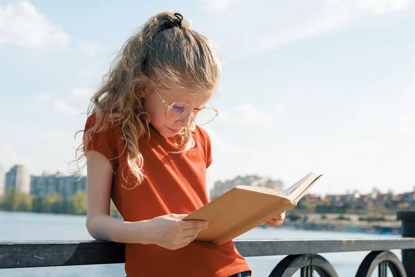 Открытый портрет маленькой школьницы с книгой, девочки 7, 8 лет с очками, читающей учебник — стоковое фото