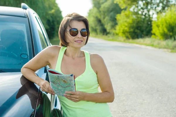 Outdoor summer portrait of mature woman with a map on the road near the car — Stock Photo, Image