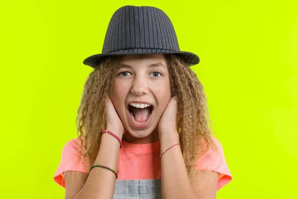 Sorprendida chica adolescente feliz con el pelo rizado en el sombrero mirando a la cámara con la boca abierta sobre fondo de estudio amarillo — Foto de Stock