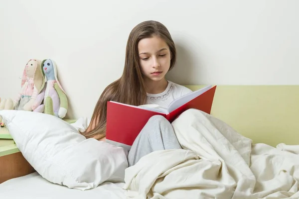 Девочка-подросток 10 лет читает школьную тетрадь на кровати. Фон интерьера детской комнаты — стоковое фото